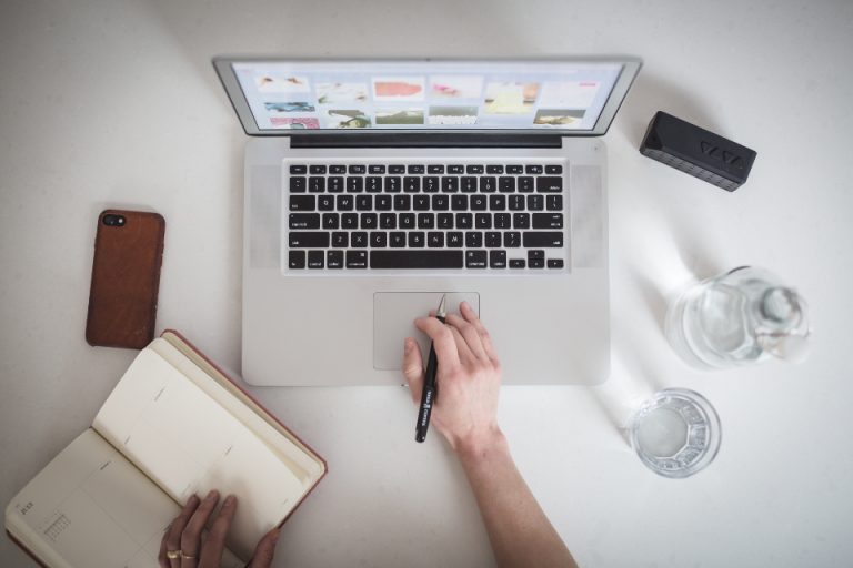 Persona al lavoro su un computer portatile, con smartphone e taccuino sulla scrivania